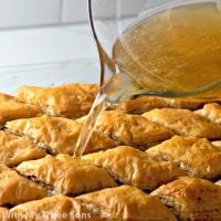 Freshly-baked baklava being topped with a golden honey syrup.