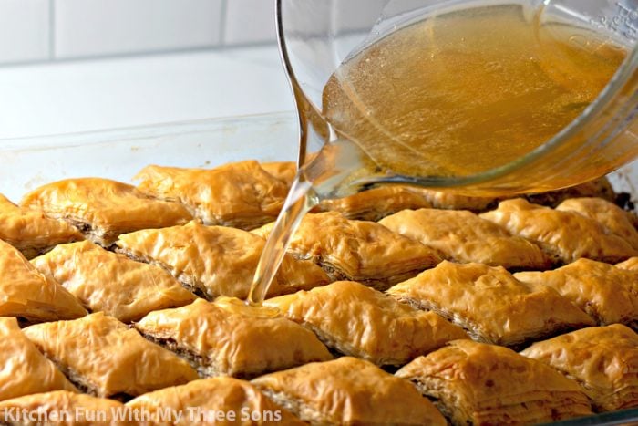 Freshly-baked baklava being topped with a golden honey syrup.