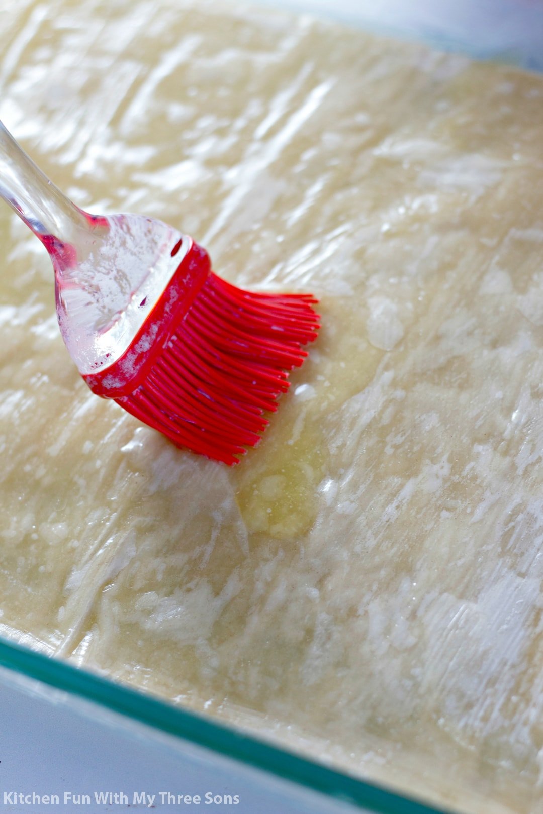 A stack of phyllo sheets being brushed with melted butter in a backing dish.