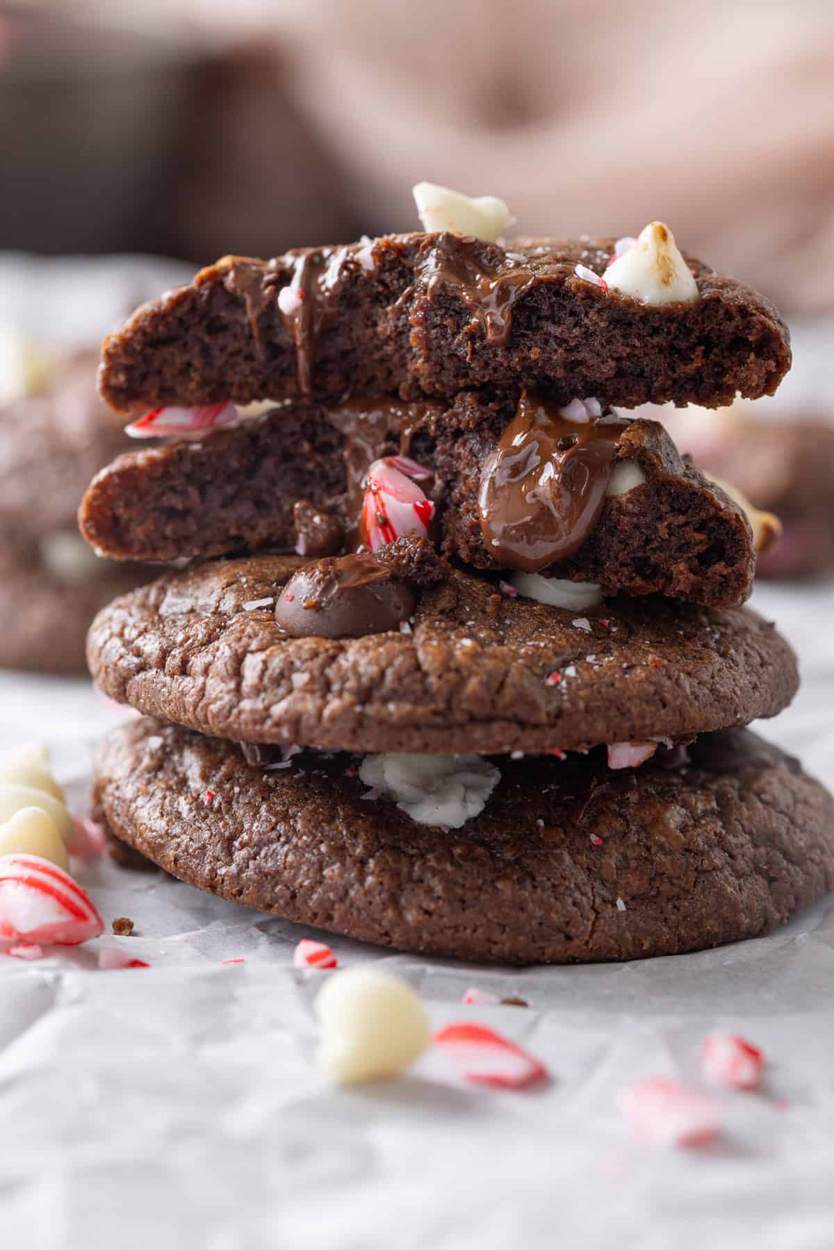 These Chocolate Peppermint Cookies are loaded with semi-sweet, white, and dark chocolate plus crushed peppermint. Soft & chewy! A stack of three chocolate peppermint cookies, one broke in half to show the inside.