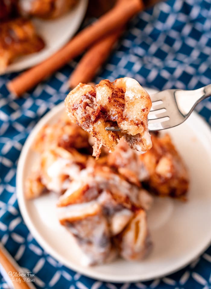 A forkful of Cinnamon Roll casserole held over a plate, with cinnamon sticks in the background.