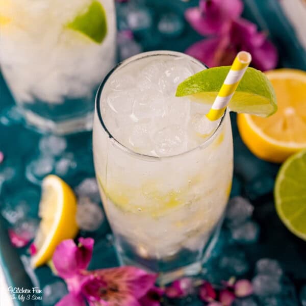 Overhead view of vodka tonic cocktails in two highball glasses garnished with lime wedges and a yellow straws.