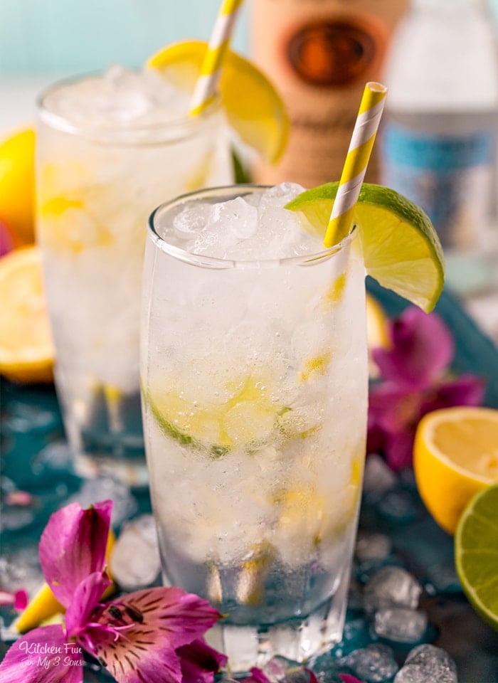 Vodka tonic cocktails in two highball glasses garnished with lime wedges and a yellow straws.