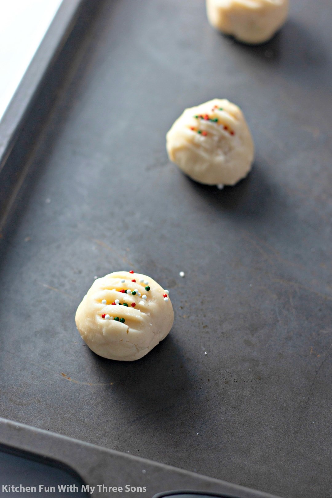 Whipped shortbread cookies topped with sprinkles on a metal baking sheet.