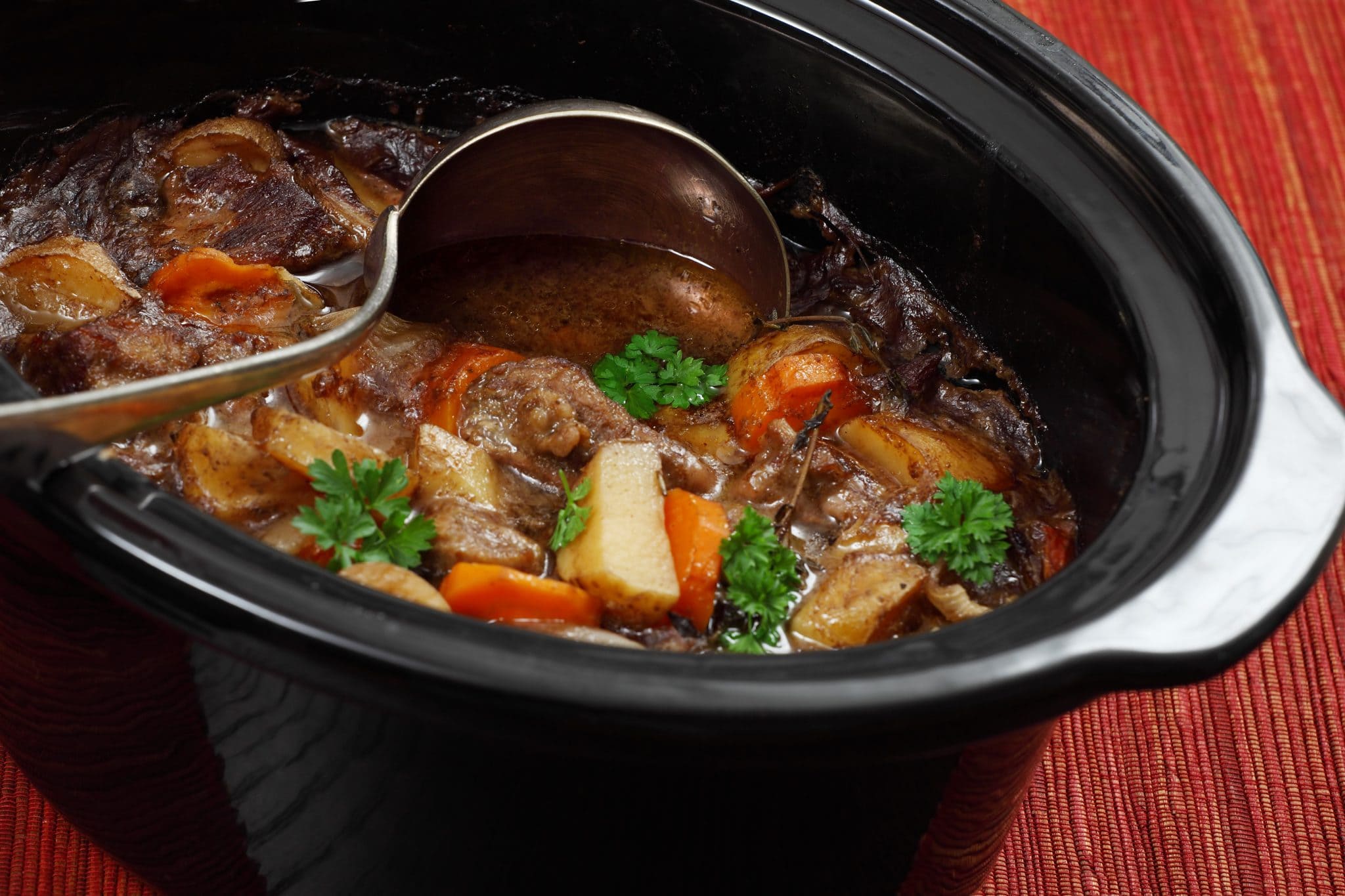 Homemade beef stew inside of a Crock Pot with a large ladle digging in