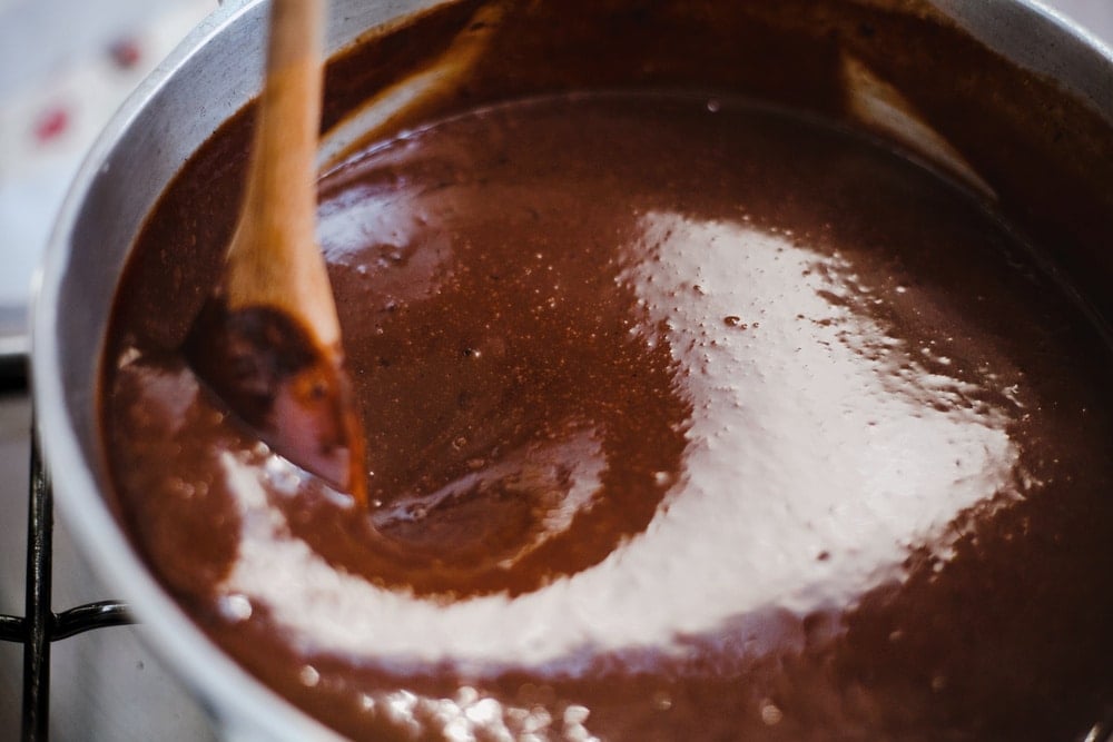 Chocolate fudge in a bowl being stirred with a wooden spoon.