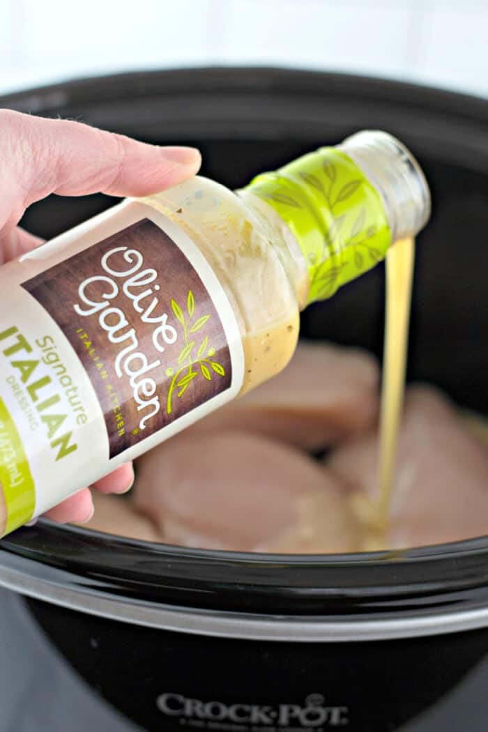 This Olive Garden Chicken Pasta is one of the easiest slow cooker dinners you'll ever make! pouring Italian dressing on chicken in the slow cooker