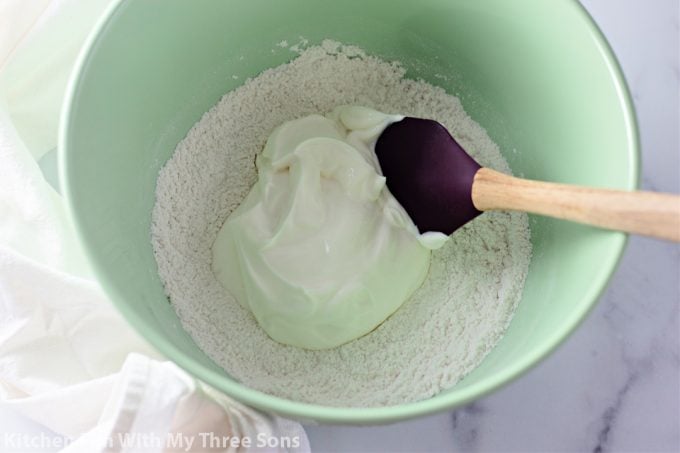 stirring together flour and Greek yogurt in a mint green bowl