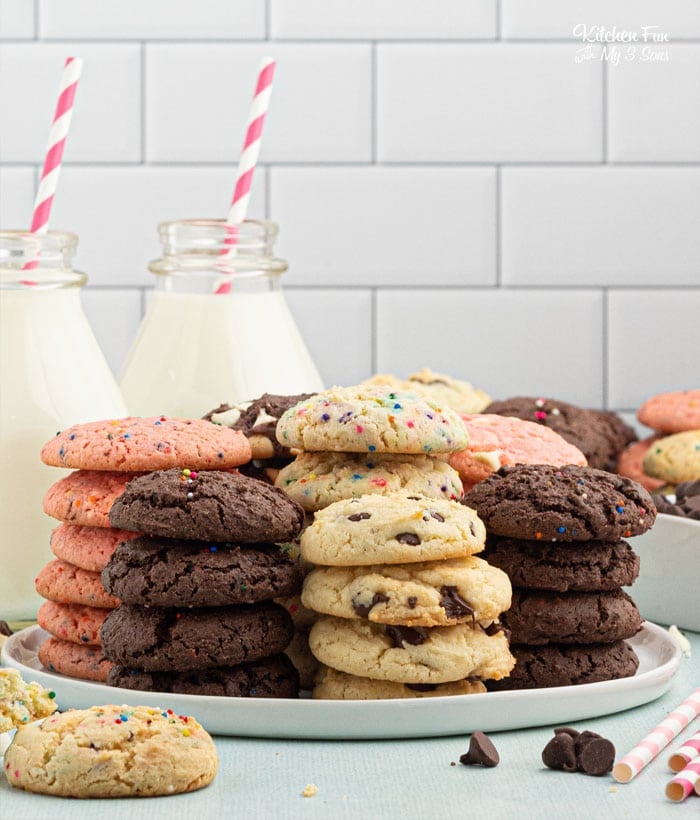 Stacks of cake mix cookies on a serving plate, with a white rectangular pan full of cookies and two jars of milk with party straws in the background.