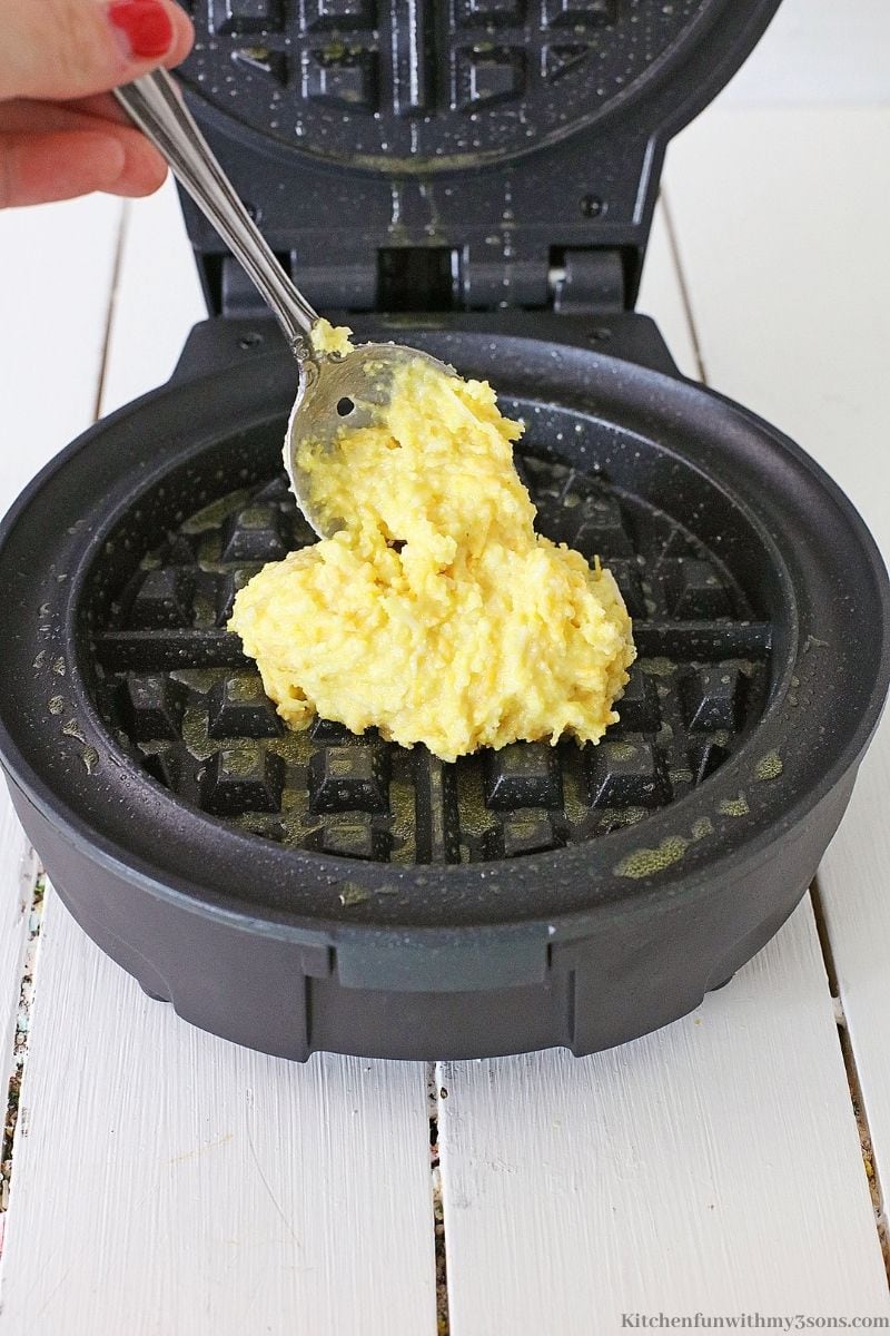 Adding the waffle mix to a grease waffle iron.