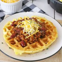Chili and cheese on top of cornbread waffles on a white plate