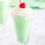 A homemade Shamrock Shake in a milkshake glass, topped with whipped cream and a cherry.