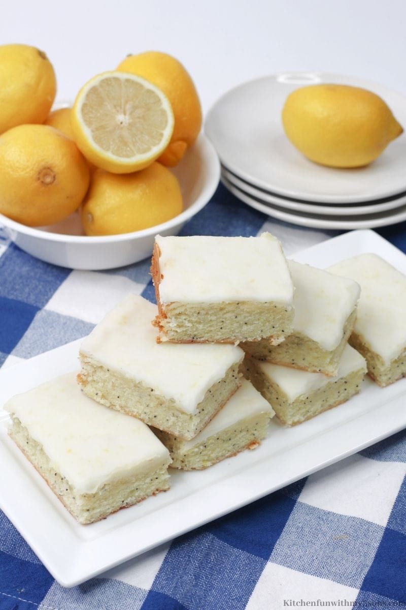 Lemon Poppy Seed Bars on a blue and white checkers cloth with extra lemons around them.