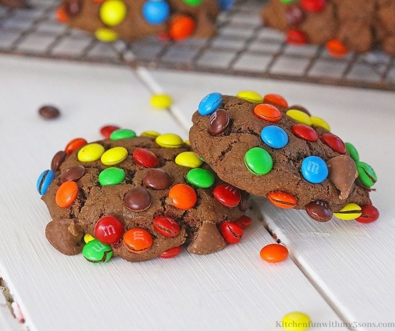 Two cookies on a white table with a few extra M&M's around them.
