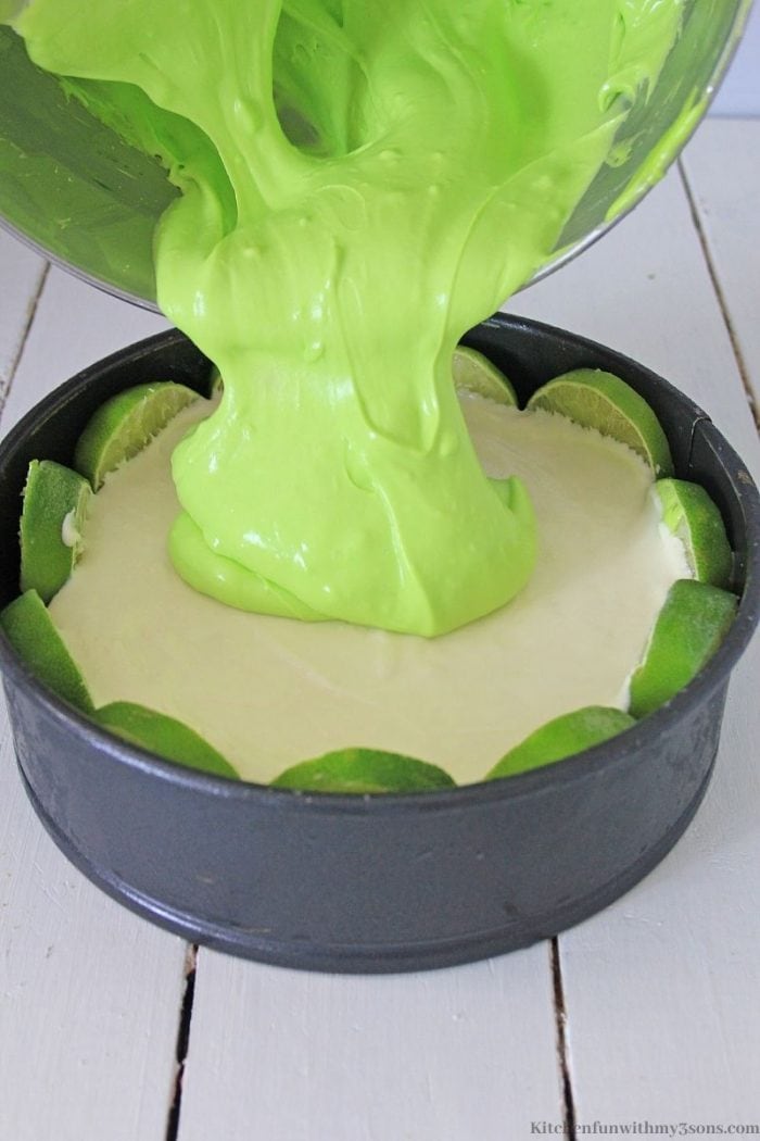 pouring the green cheesecake filling over key lime cheesecake