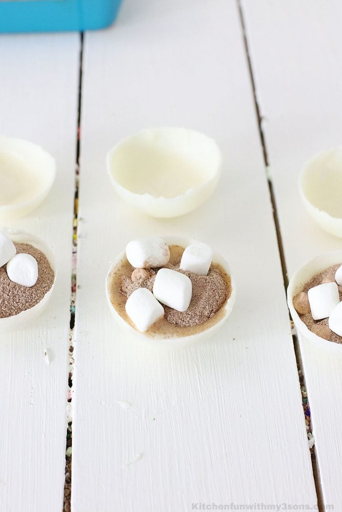 A white chocolate shell being filled with hot cocoa and mini marshmallows