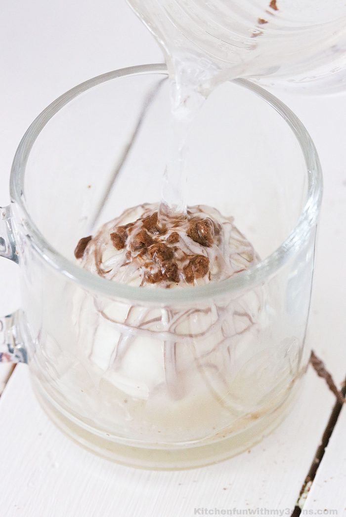 pouring milk over cocoa bomb in a glass mug