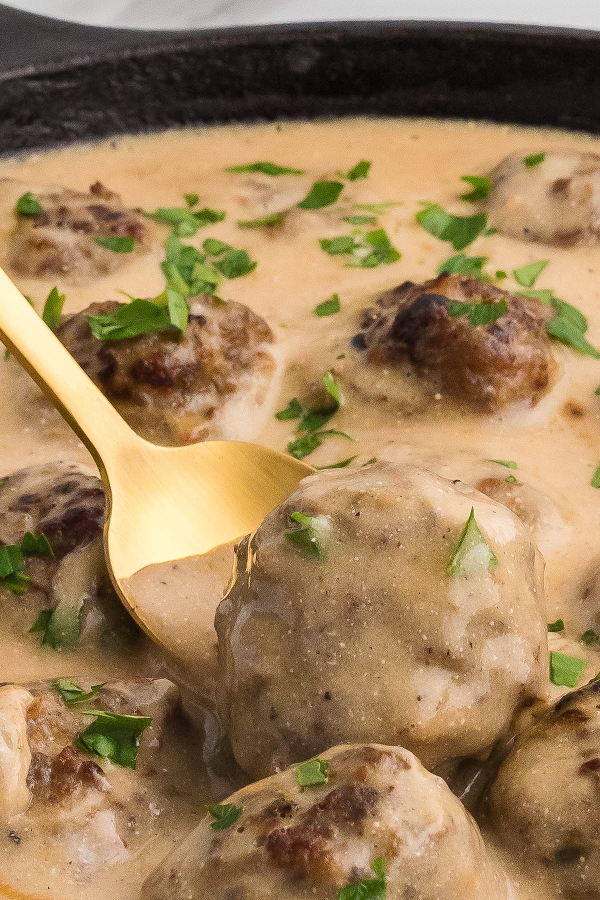 A spoon pulling a Swedish meatball from a skillet
