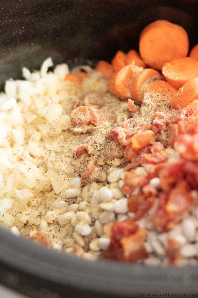 Adding the herbs, spices, and bacon into the slow cooker.