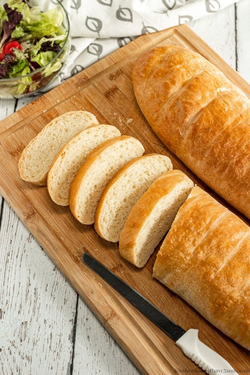 The sliced French bread with a bread knife beside it with a side salad.