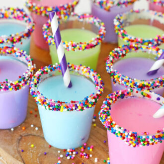 Assorted colorful birthday cake shots rimmed with frosting and rainbow sprinkles.