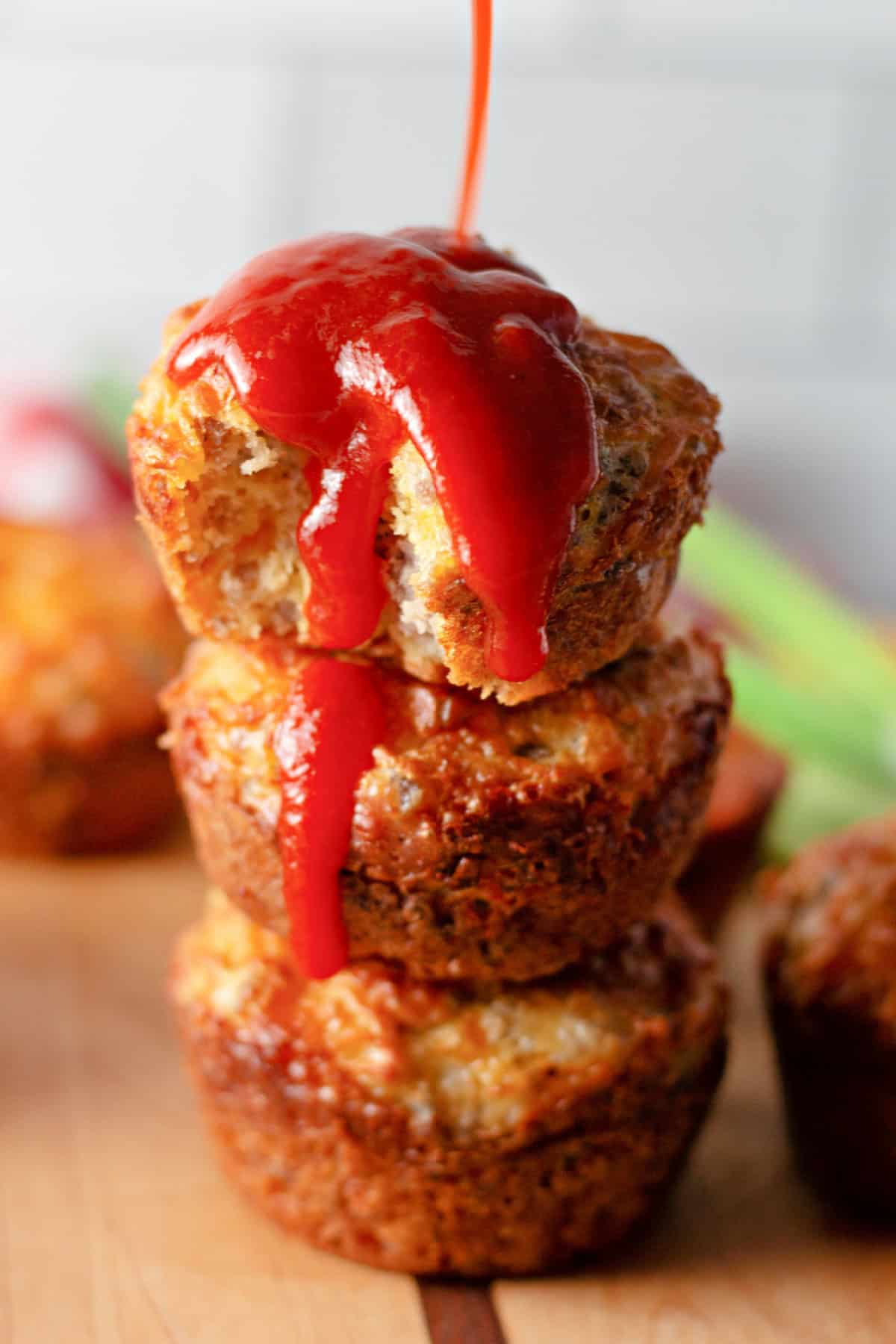 These easy Sausage Breakfast Muffins are packed with savory sausage, fluffy eggs, melted cheddar cheese, and Bisquick for the ultimate grab-and-go breakfast. hot sauce being poured on top of stacked sausage breakfast muffins
