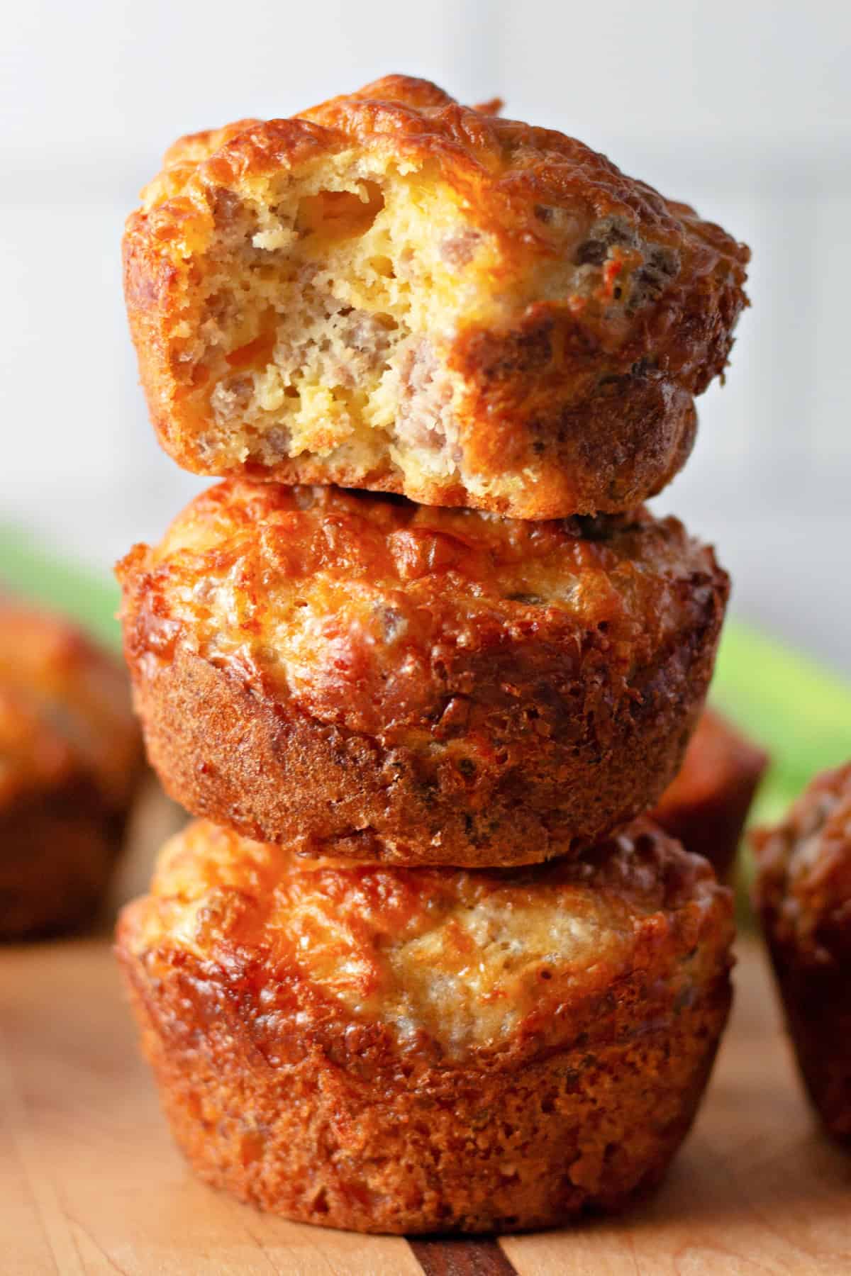 These easy Sausage Breakfast Muffins are packed with savory sausage, fluffy eggs, melted cheddar cheese, and Bisquick for the ultimate grab-and-go breakfast. Sausage breakfast muffins stacked with a bite taken out showing the inside.