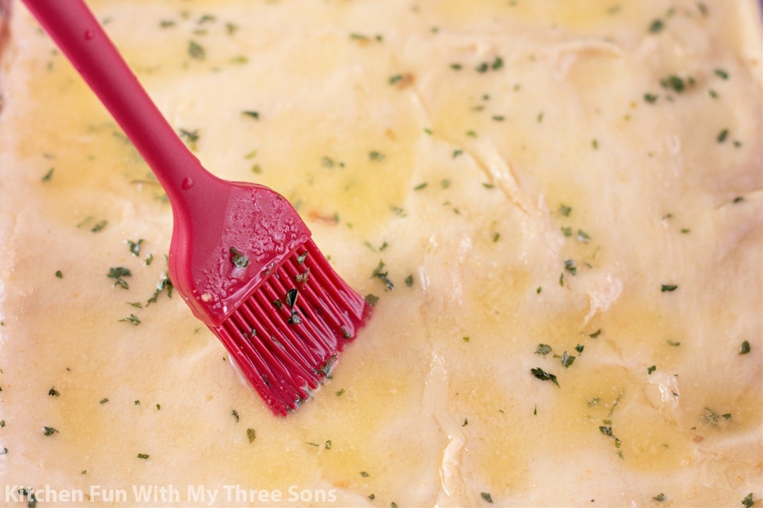 brushing melted butter over crescent roll dough.