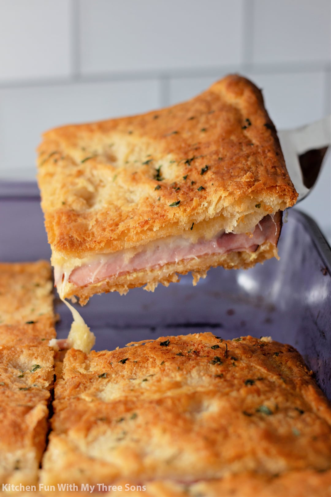 picking up a piece of Baked Ham and Cheese Sandwiches with a spatula.