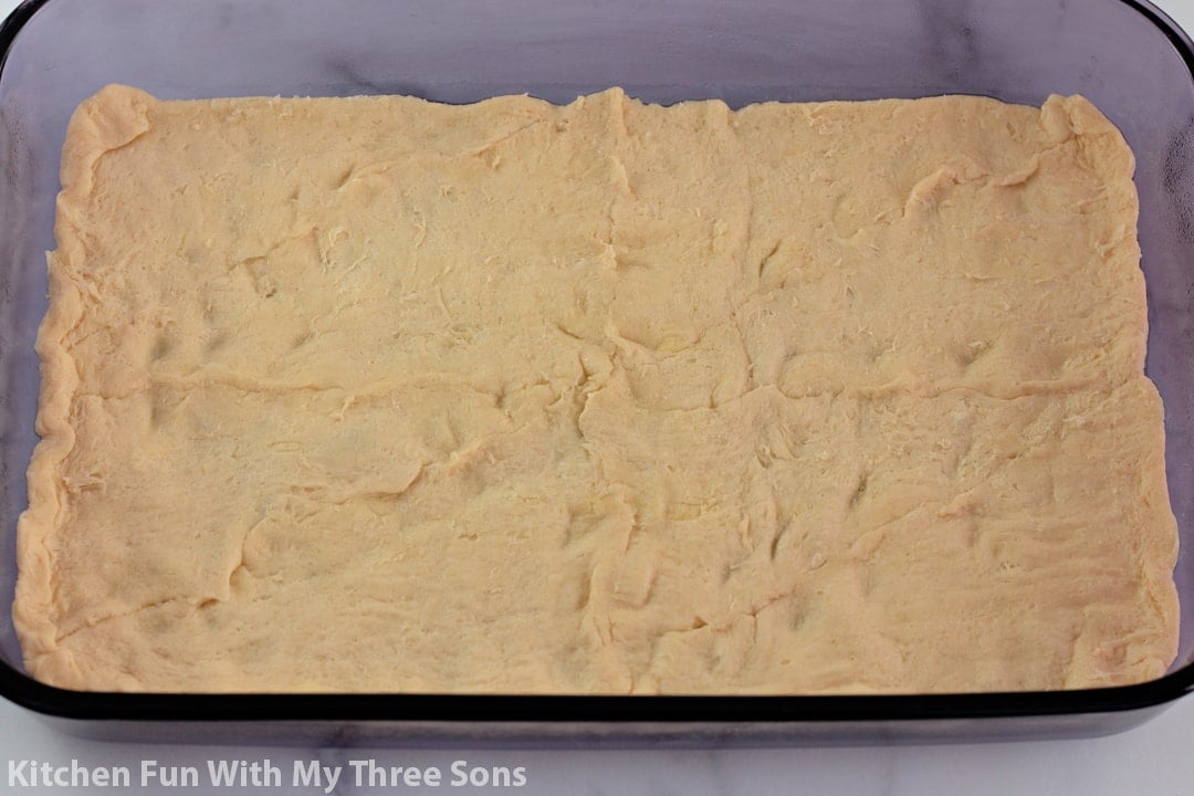 pressing crescent roll dough into a baking dish.