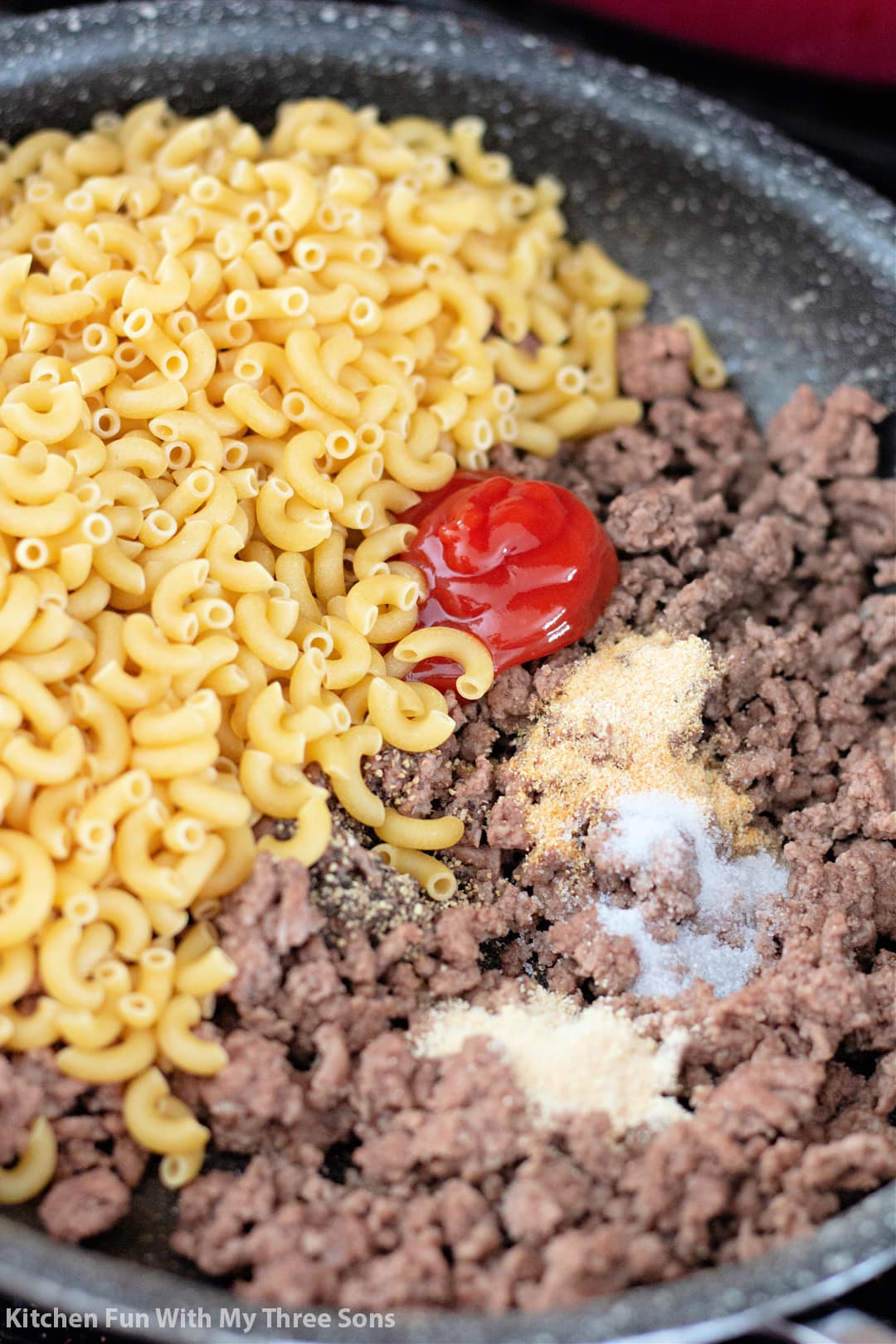 Uncooked macaroni noodles inside of a skillet with ground beef, ketchup and various seasonings
