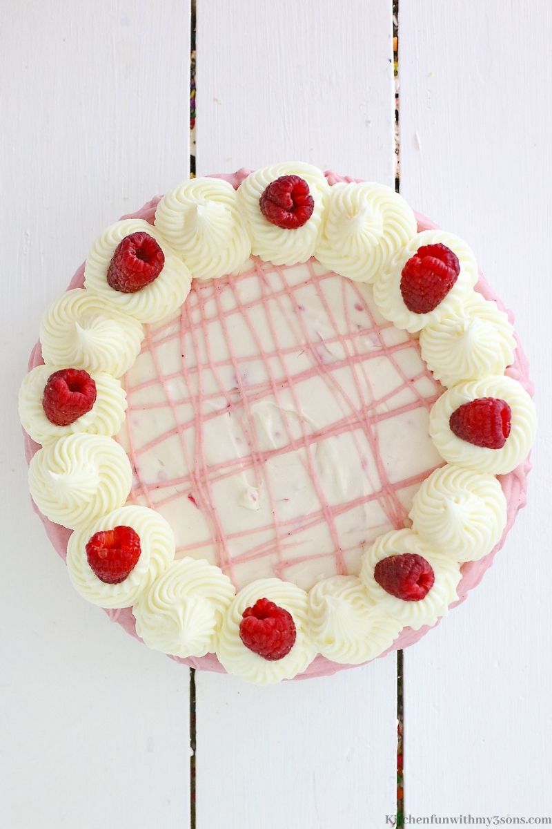 The whole uncut White Chocolate Raspberry Cheesecake on a white wooden table.