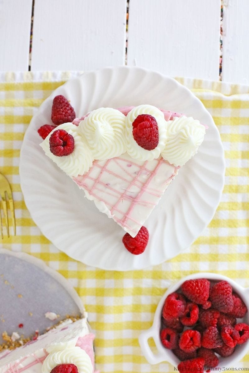 A piece of the cheesecake on a yellow cloth with extra raspberries on the side.