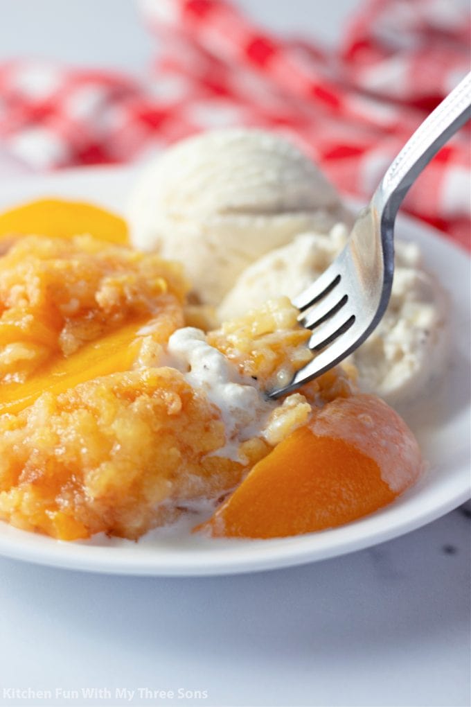 Easy Peach Dump Cake with a fork and vanilla ice cream.