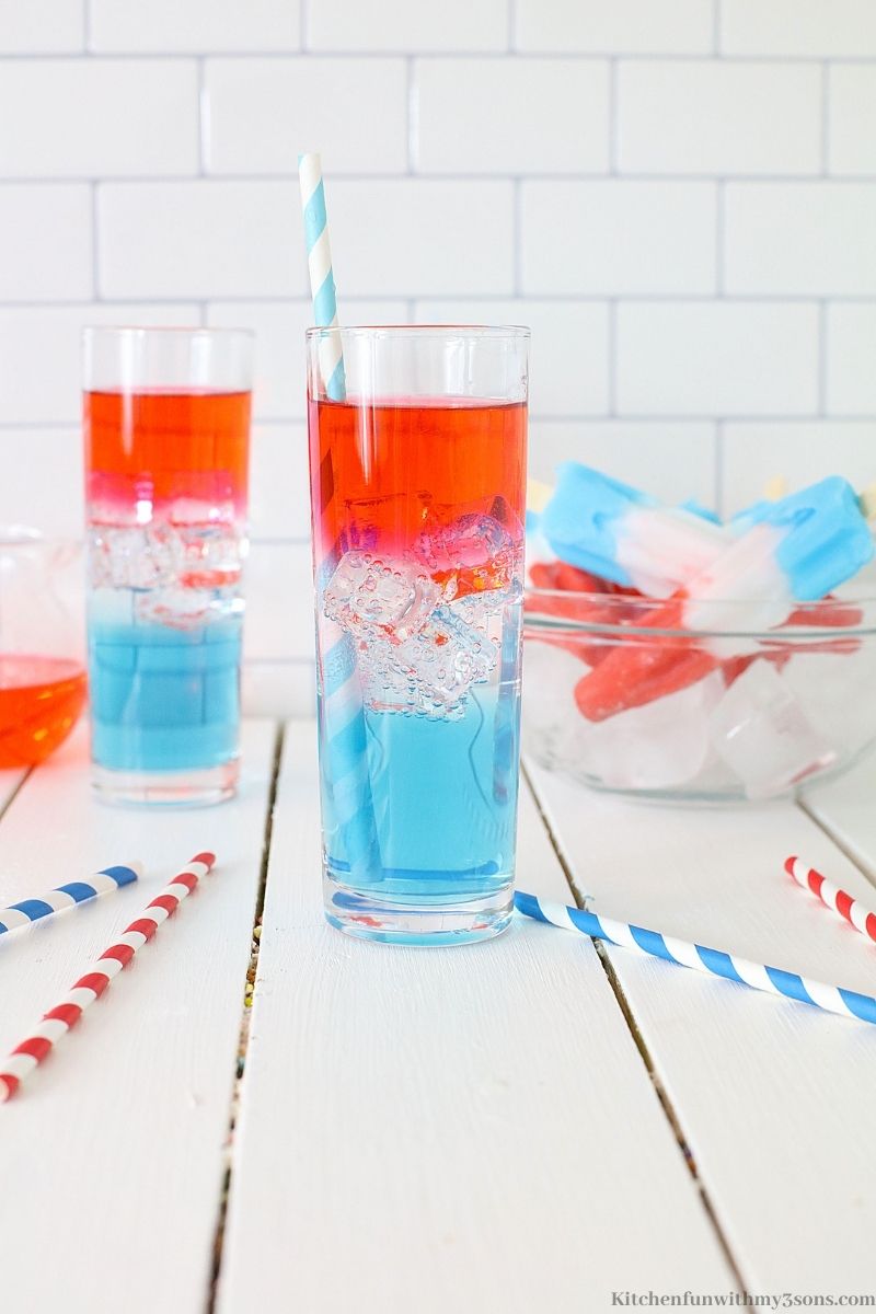 Two glasses of Rocket Pop Vodka Cocktail on a white wooden table with straws.
