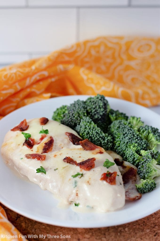 Cheesy Smothered Chicken with Bacon on a white plate with broccoli.