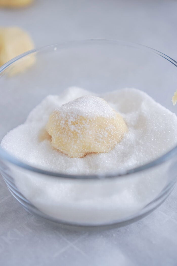 A ball of sugar cookie dough being rolled in sugar