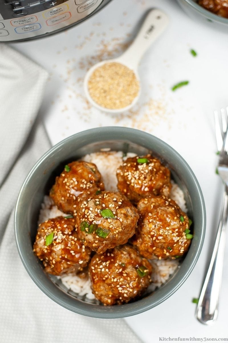 The meatballs in a serving bowl with a 1/4 cup of sesame seeds in a measuring cup on the side.