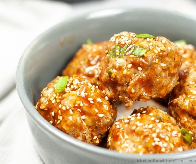 A close up of the Asian Meatballs in a bowl garnished with sesame seeds and chopped green onions.