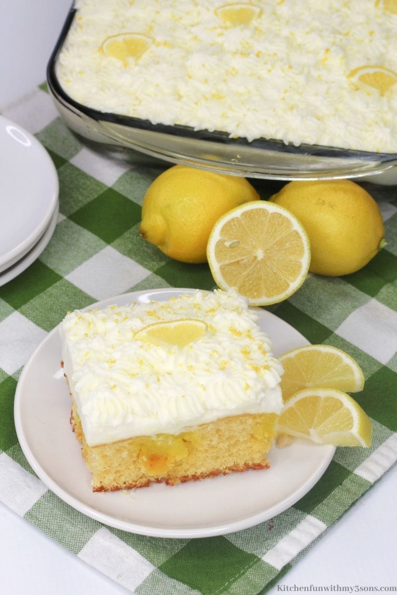 A piece of the lemon poke cake on a white and green checkered cloth.