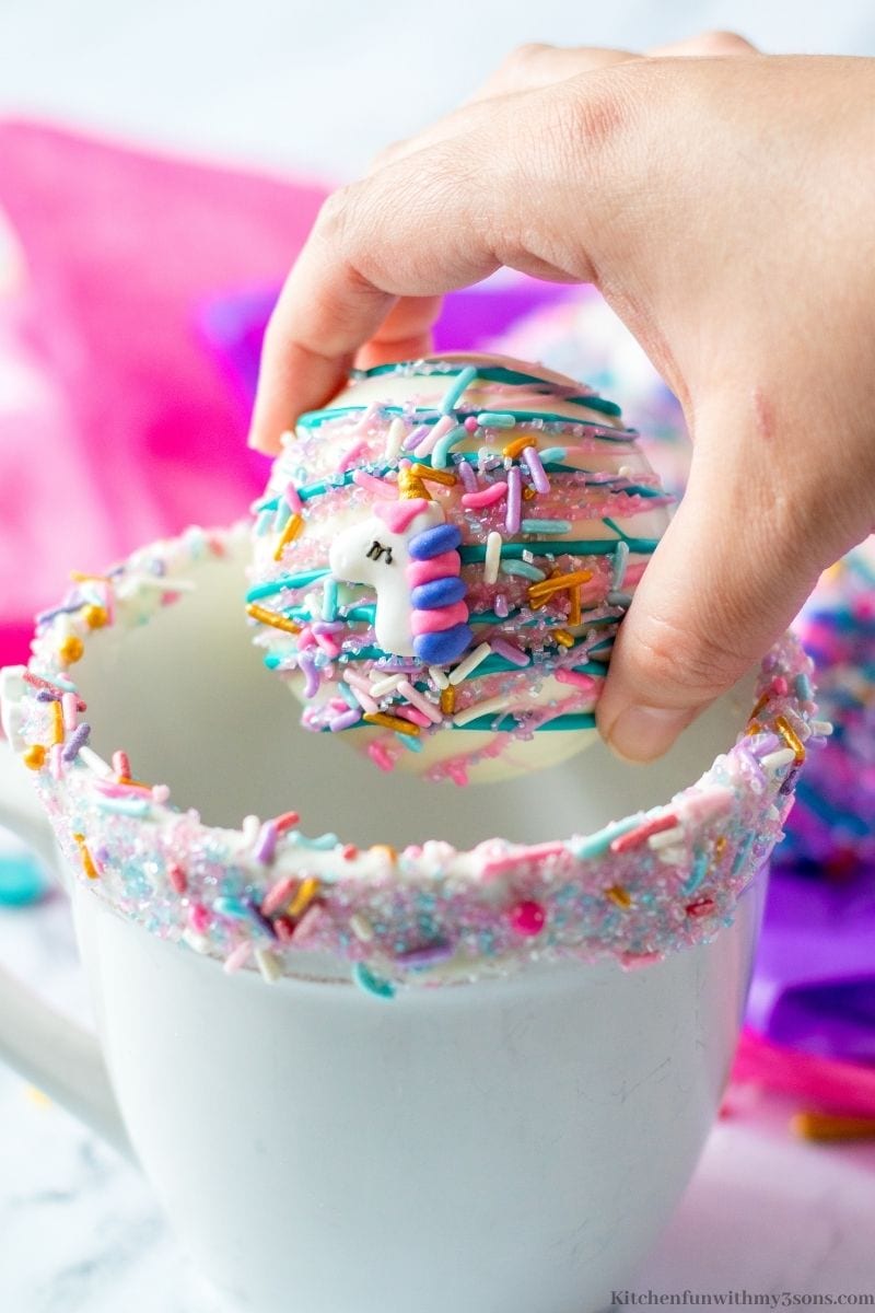 A hand getting ready to place a Unicorn Hot Chocolate Bombs in a mug.