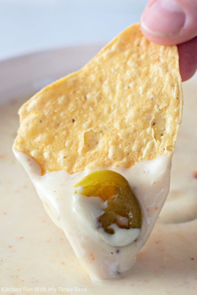 dipping a chip in The Best White Queso Dip.