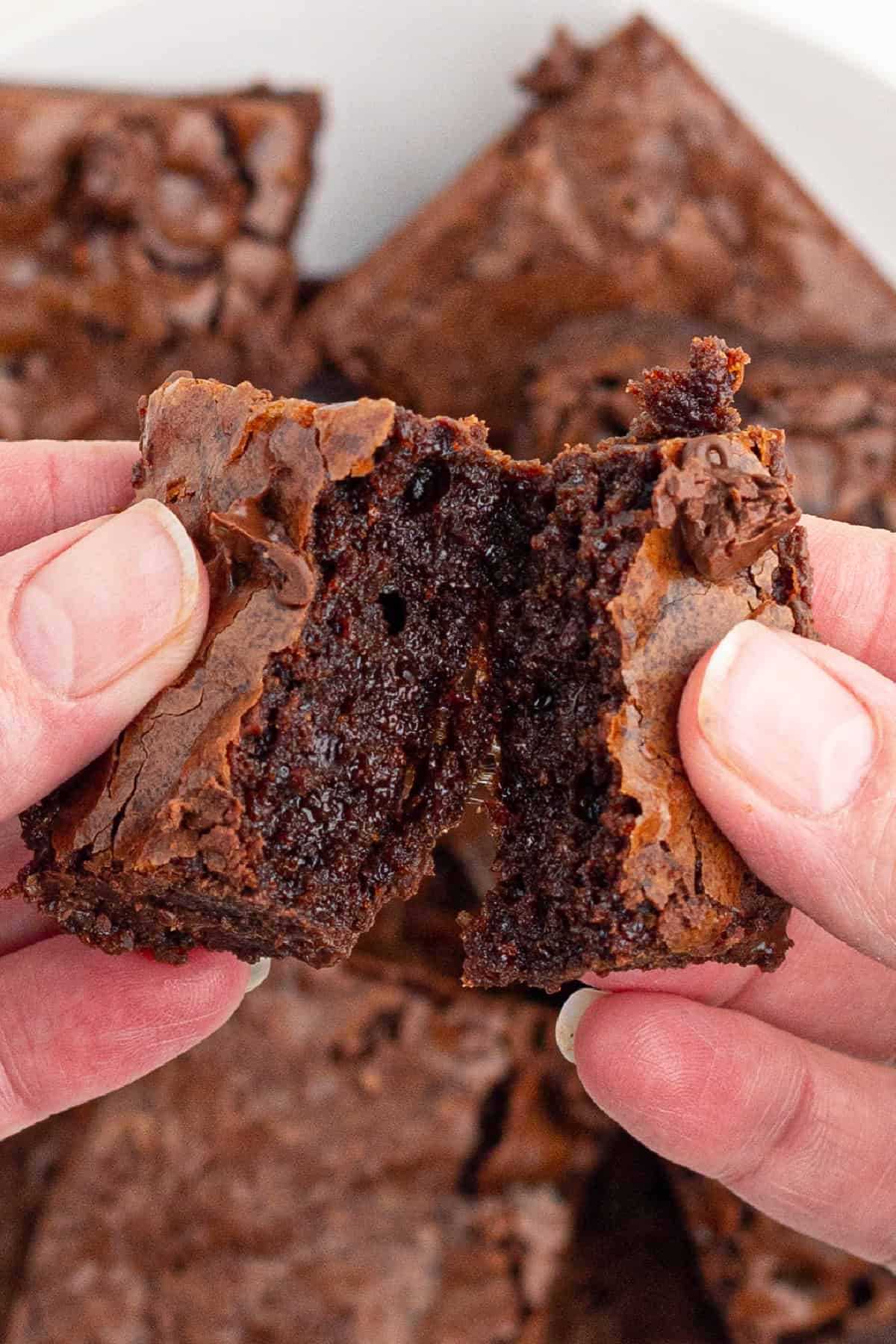 Resulting in decadently chewy, fudgy brownies with a perfectly crackly top, this is by far the Best Brownie Recipe I've ever tried. breaking open a fudgy brownie showing the inside