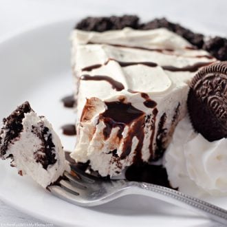 A slice of no-bake Oreo pie on a plate, drizzled with chocolate sauce next to a forkful of pie in the foreground.