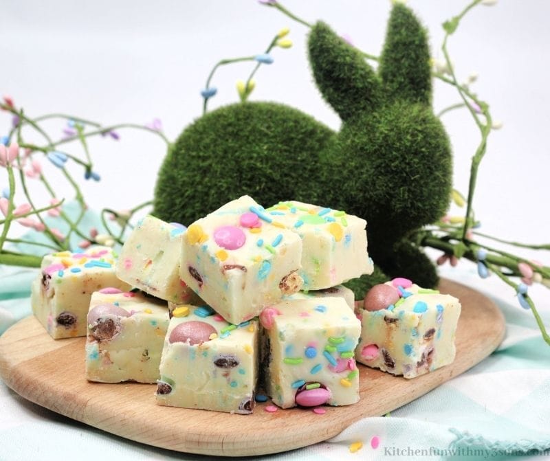 The fudge on a wooden cutting board with a bunny shaped bush decoration in the back.