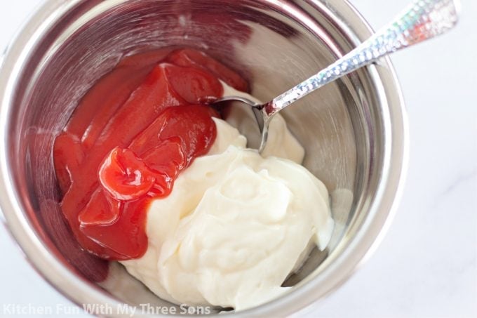 mixing together ketchup and mayonnaise in a metal bowl.