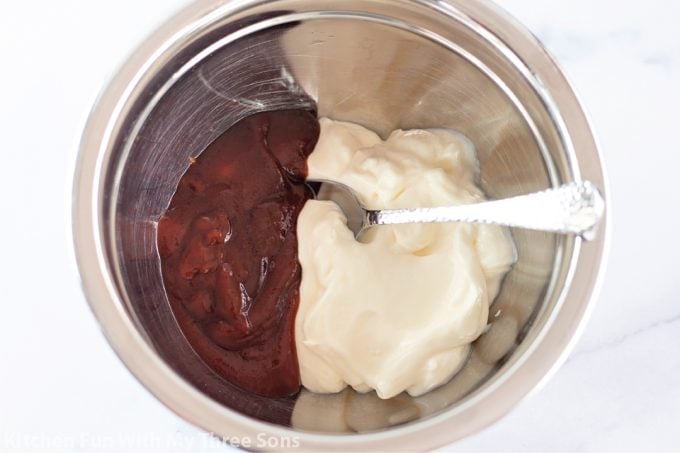mixing together BBQ sauce and mayonnaise in a metal bowl.