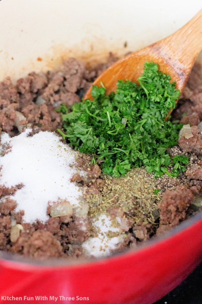 adding fresh parsley and seasonings to cooking meat in the pot.