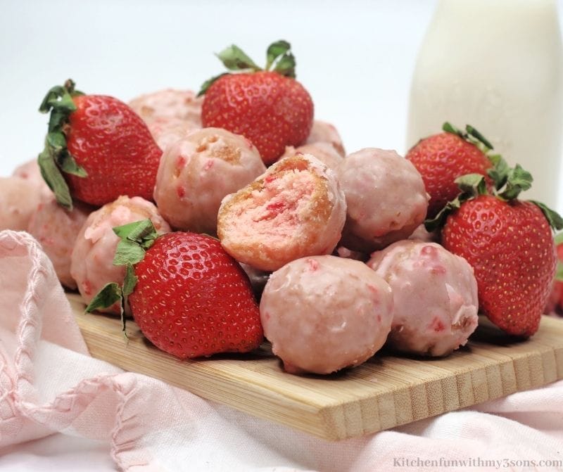 Donut holes on a wooden cutting board with more strawberries mixed in.