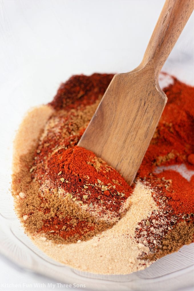 mixing spices together in a clear bowl with a wooden spoon.